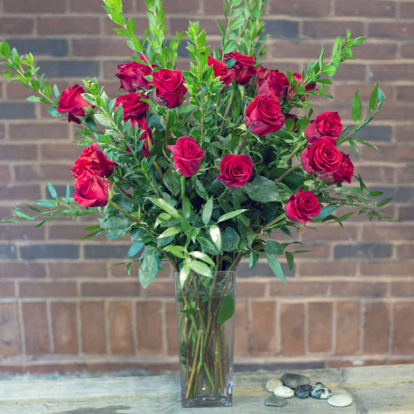 Red roses arranged in a tall clear glass vase