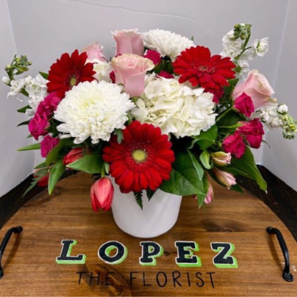 Bouquet of red gerbera daisies, pink roses, and white blooms in a white vase