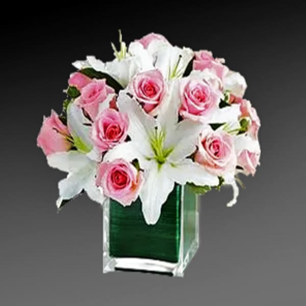 Pink roses and white lilies arranged in a clear square vase