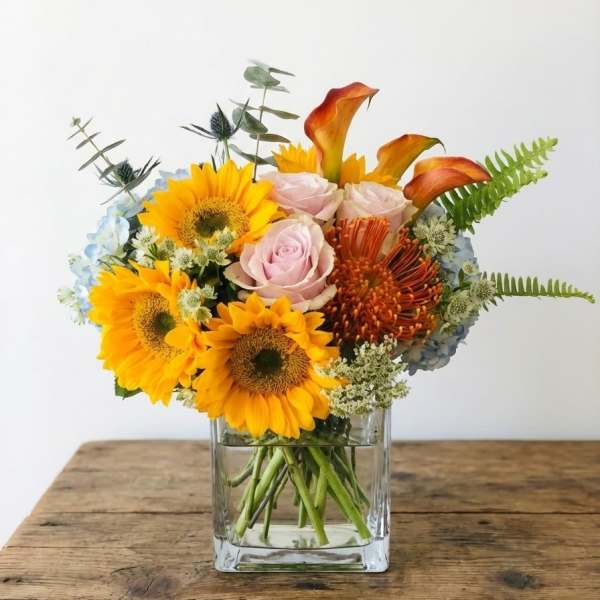 Bouquet of sunflowers, roses, and orange calla lilies in a glass vase