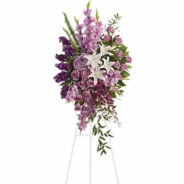 Tall purple and lavender standing spray with white lilies on a white easel.