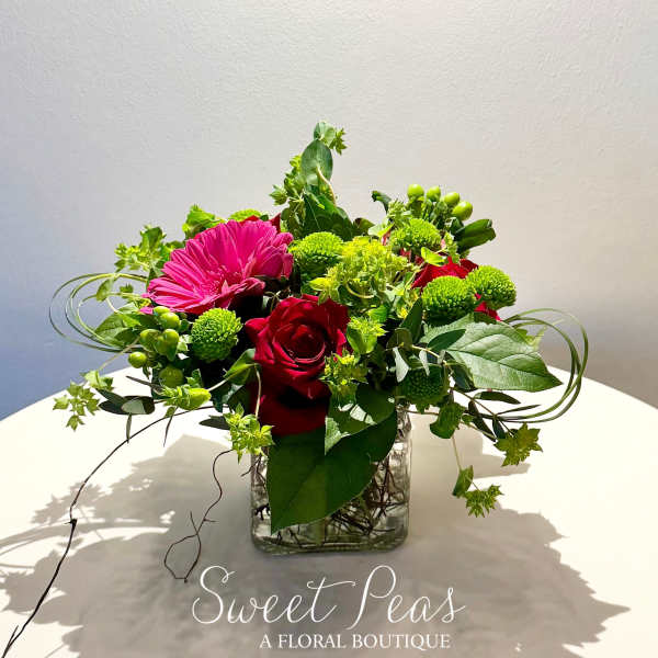 Mixed floral arrangement with red roses and a pink gerbera daisy in a glass vase