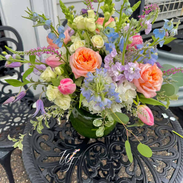 Mixed bouquet of peach, pink, blue, and lavender flowers in a green vase