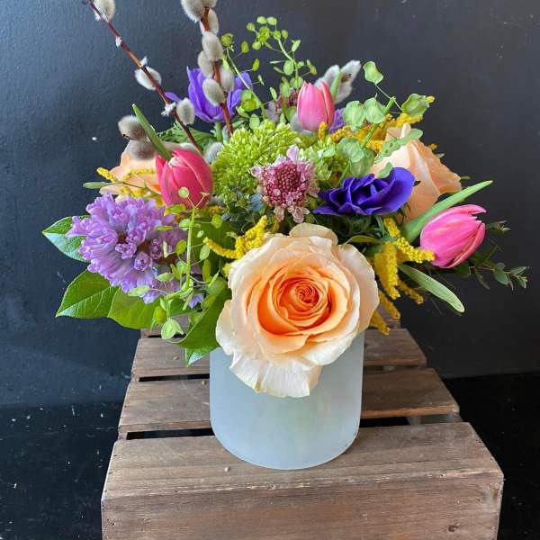 Mixed bouquet in a frosted vase with peach roses, pink tulips, and purple blooms