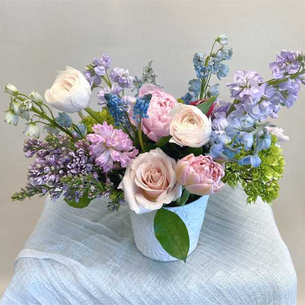 Pastel bouquet of roses, peonies, and blue-purple blooms in a white vase