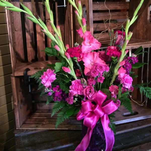 Pink floral arrangement with tall gladiolus in a dark vase and ribbon