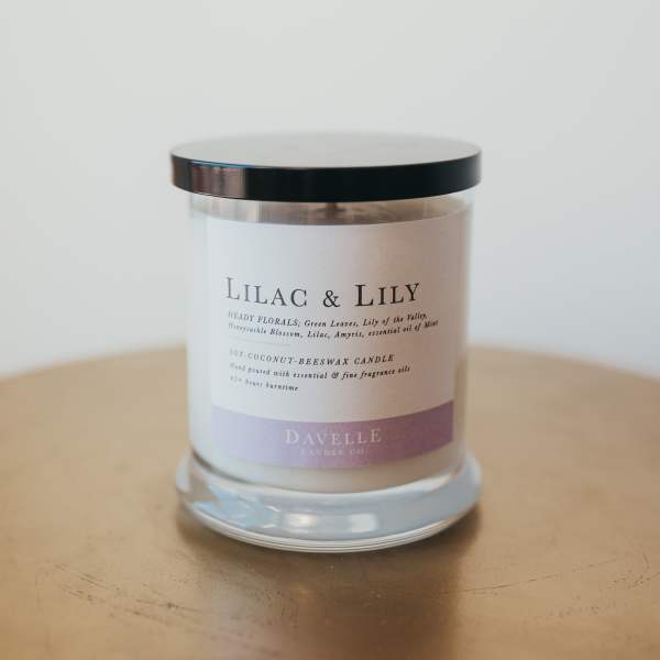 A lilac and lily scented candle in a glass jar with a black lid