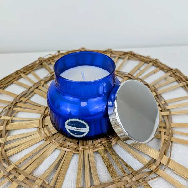 Blue glass candle jar with a silver lid on a woven mat