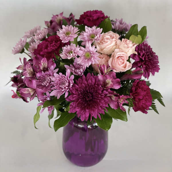 Pink and purple mixed bouquet in a purple glass vase