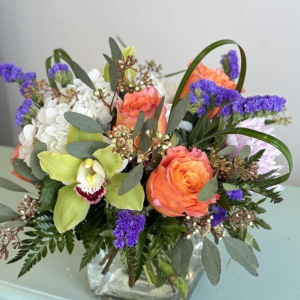 Mixed bouquet in a square glass vase with orange roses and green orchids