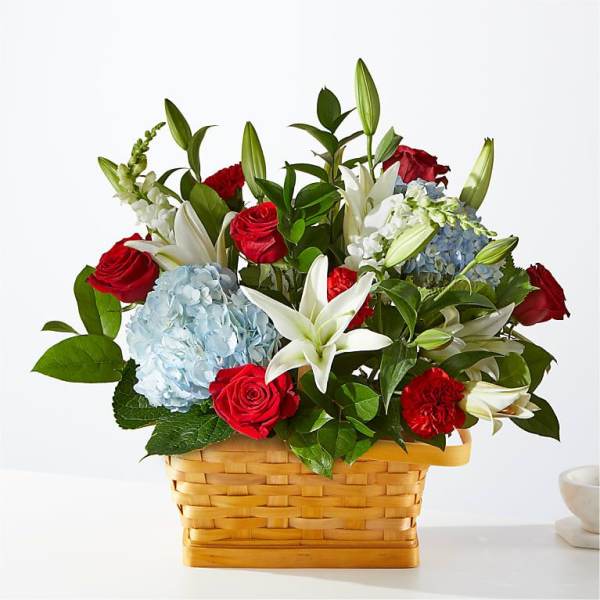 Basket arrangement of red roses, white lilies, and blue hydrangeas