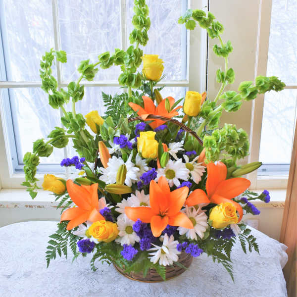 Basket arrangement of orange lilies, yellow roses, and white daisies