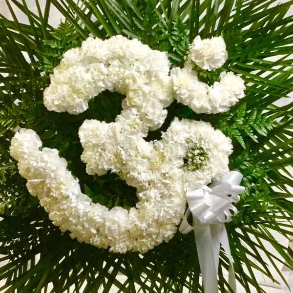 White floral heart wreath with a ribbon bow on a green palm backdrop