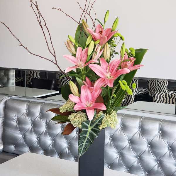 Pink lilies arranged in a tall black vase with branches