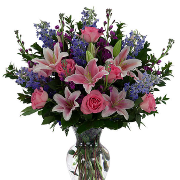 Pink lilies and roses with blue flowers in a clear glass vase