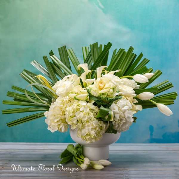 White floral arrangement in a white vase with fan-shaped palm leaves