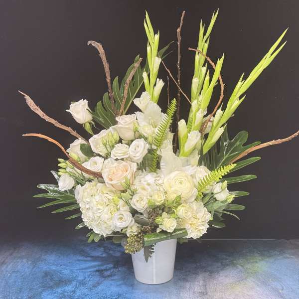 Tall white floral arrangement in a white vase with green accents