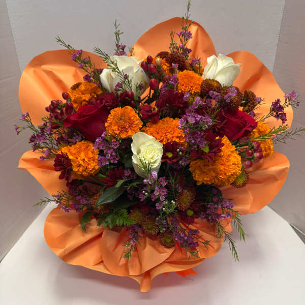 Bright bouquet of orange marigolds, red and white roses, and purple blooms wrapped in orange tissue