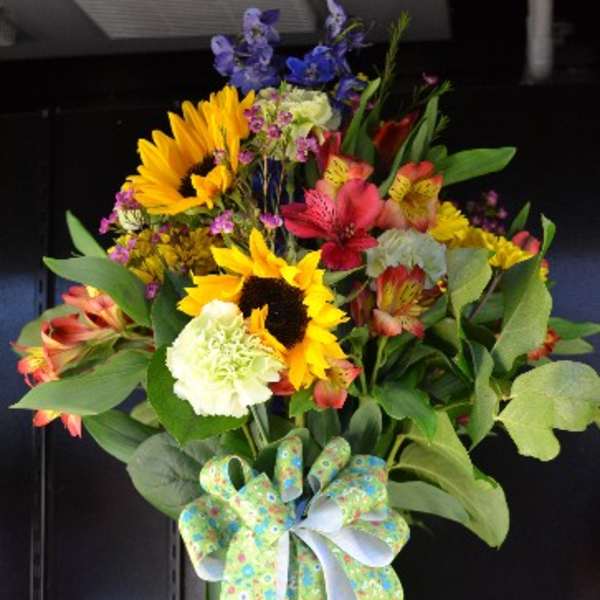 Tall mixed bouquet with sunflowers, lilies, and a decorative bow in a green vase