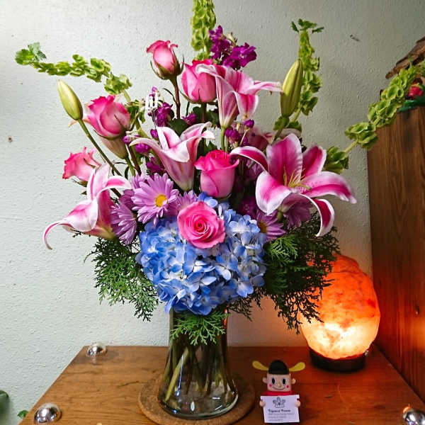 Pink lilies and roses with blue hydrangea in a glass vase