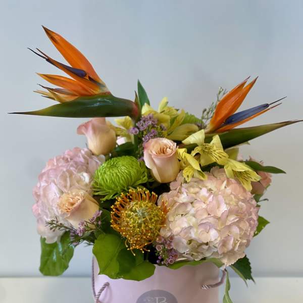 Pink floral arrangement in a round box with orange bird-of-paradise blooms