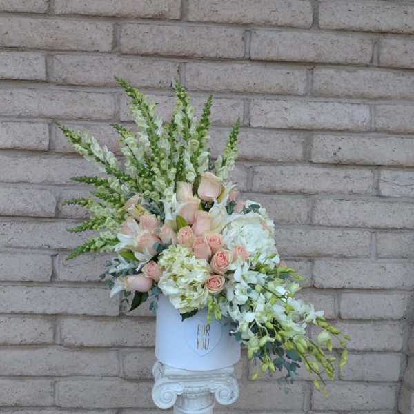 Pastel floral arrangement in a white hatbox on a pedestal