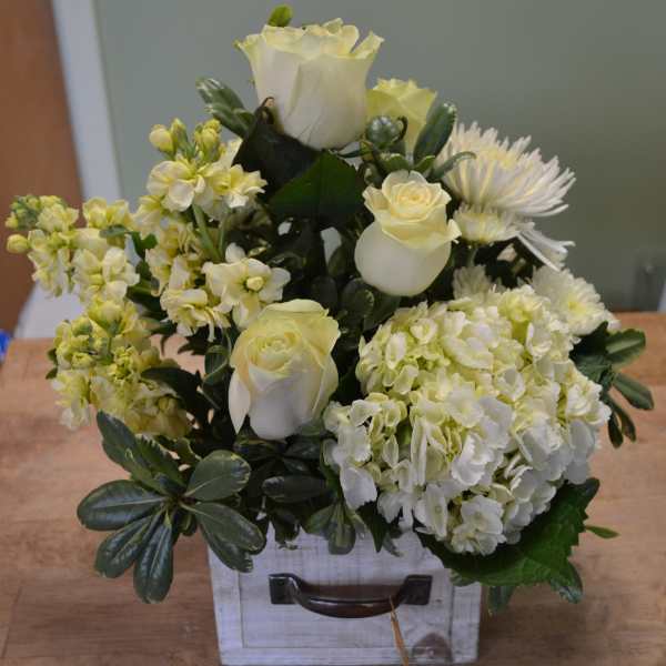 White roses and pale yellow flowers arranged in a white box.