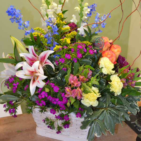 Colorful mixed flower arrangement in a white basket with tall curly branches
