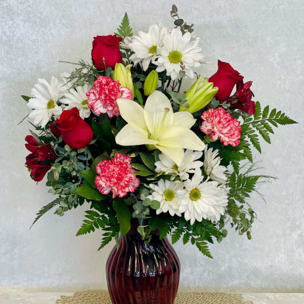 Mixed bouquet of red roses, white lilies, and daisies in a burgundy vase