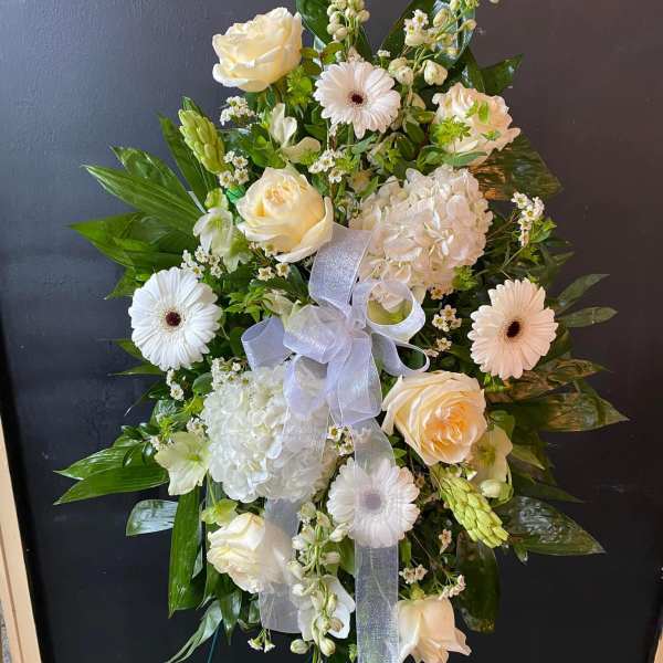 White floral standing spray with roses, gerberas, and hydrangea on an easel