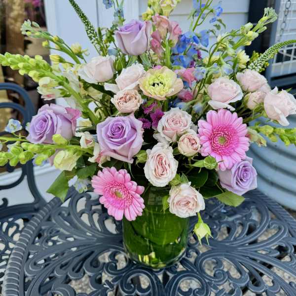 Pastel bouquet of roses, gerbera daisies, and blue delphinium in a glass vase