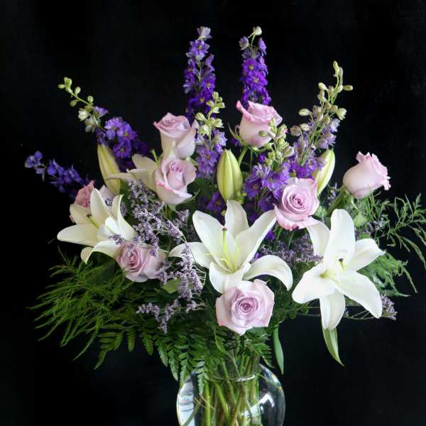 Bouquet of white lilies, pale pink roses, and purple flowers in a glass vase