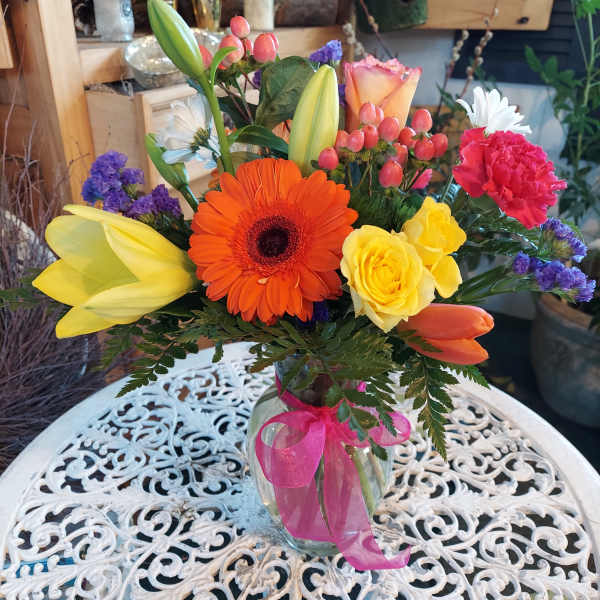 Colorful mixed bouquet in a glass vase with a pink ribbon