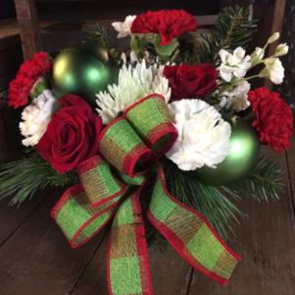 Christmas floral arrangement with red and white flowers, ornaments, and a large ribbon bow