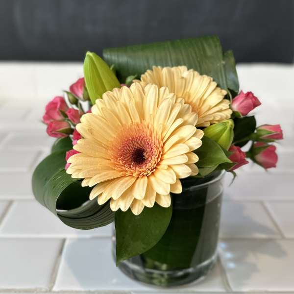 Yellow gerbera daisies and pink roses in a glass vase