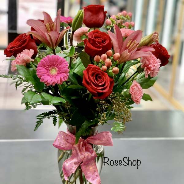 Bouquet of red roses and pink lilies in a glass vase with a pink ribbon