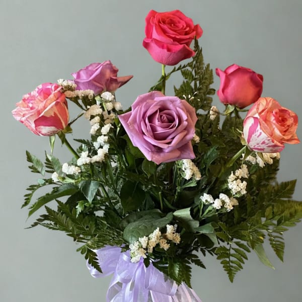 Bouquet of pink and lavender roses with white filler flowers and a purple ribbon