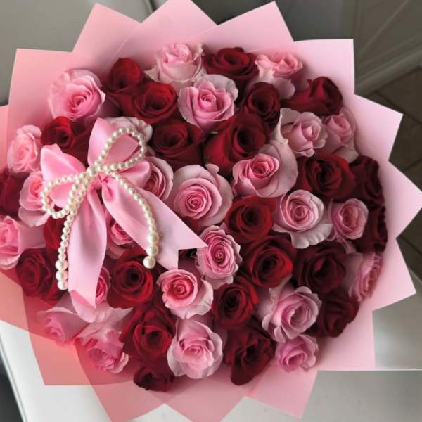 Bouquet of pink and red roses wrapped in pink paper with a pearl bow