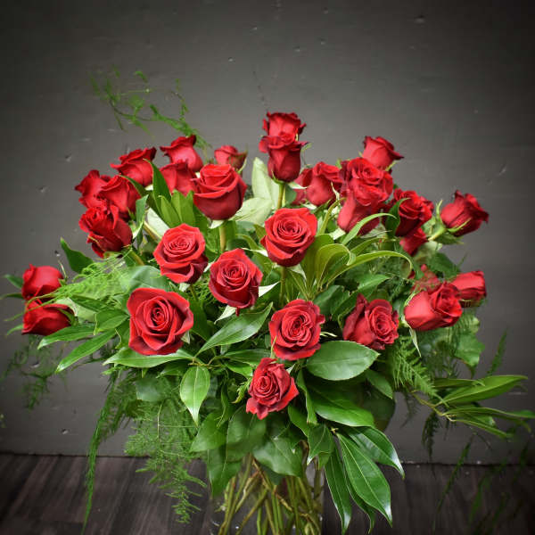 Tall arrangement of long-stemmed red roses with lush foliage in a clear glass vase