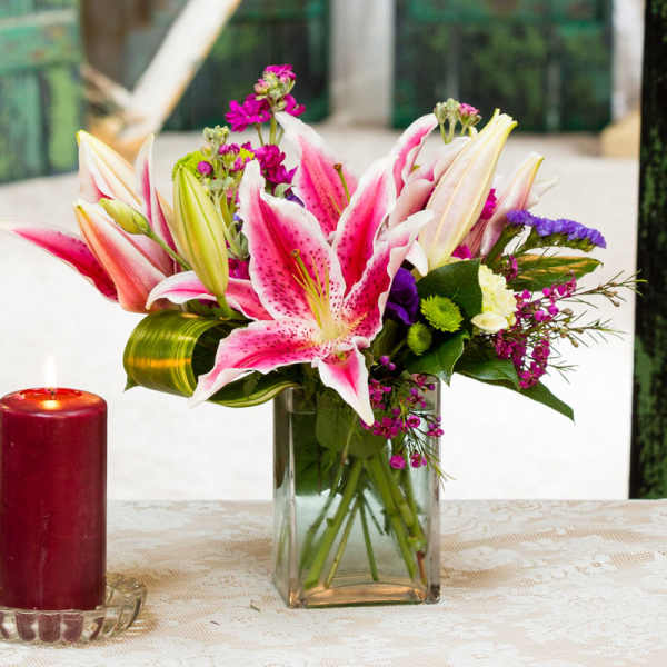 Pink and white lilies arranged in a clear glass vase beside a red candle