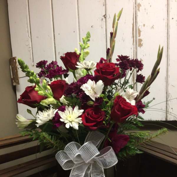 Bouquet of red roses, white daisies, and purple flowers in a glass vase with a white bow