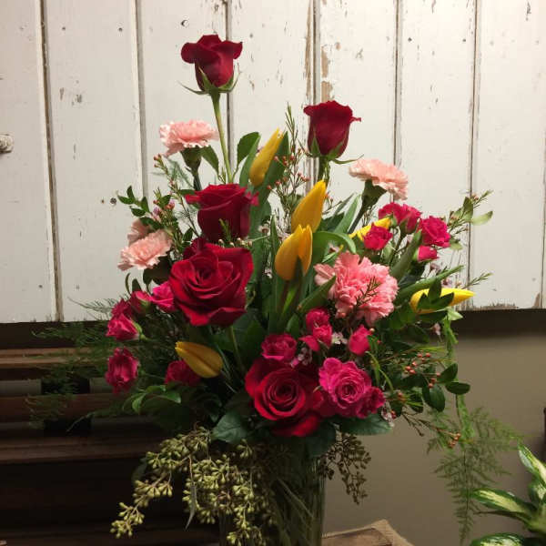 Tall bouquet of red roses, pink carnations, and yellow tulips in a glass vase