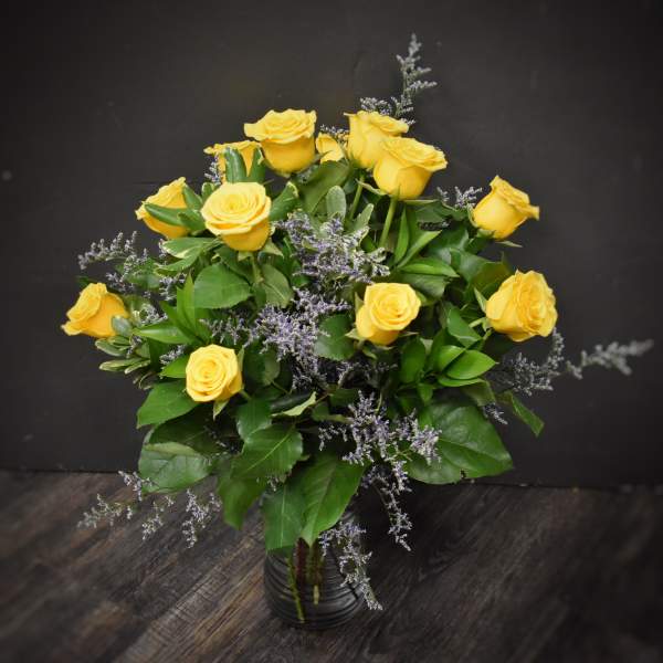 Arrangement of yellow roses with soft purple filler in a clear glass vase