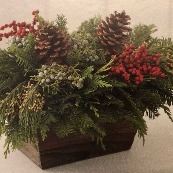 Holiday centerpiece with pinecones, evergreen branches, and red berries in a wooden container