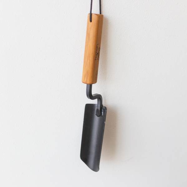 A hanging metal tool with a wooden handle against a white wall.