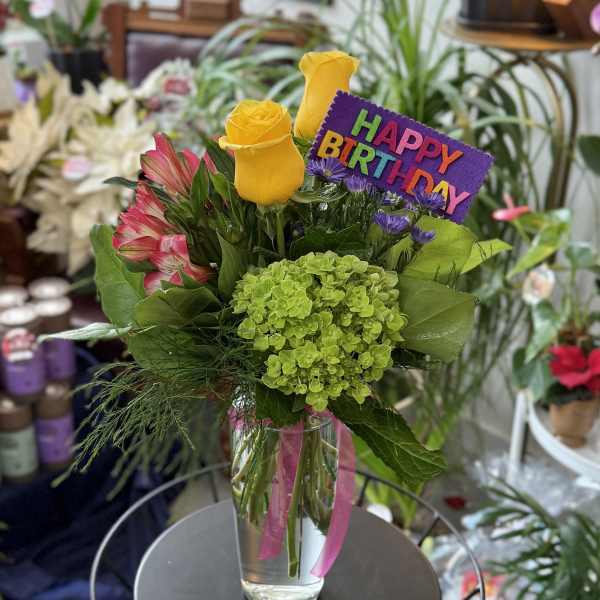 Birthday bouquet with yellow roses, pink flowers, and a purple sign in a glass vase