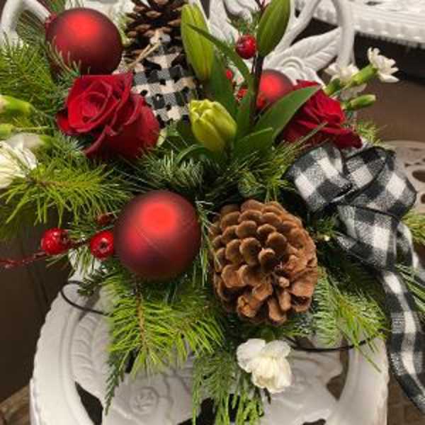 Holiday floral arrangement with red roses, pinecones, and ornaments in a white chair