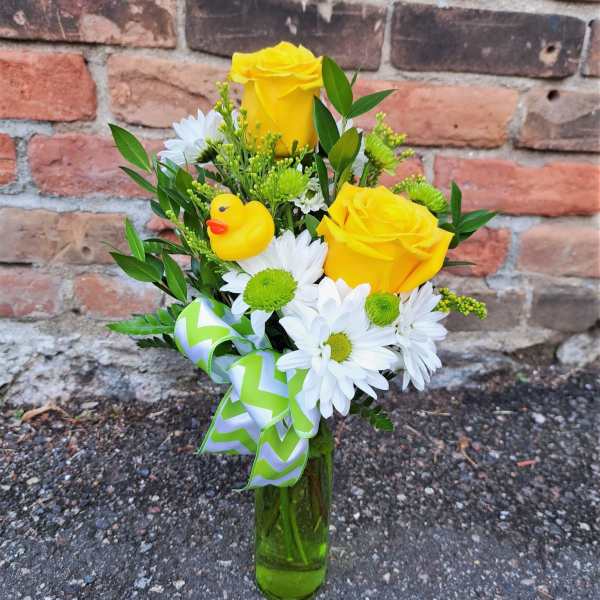 Yellow roses and white daisies in a glass vase with a duck ornament