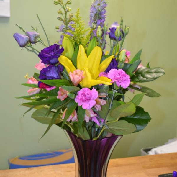 Colorful mixed bouquet in a tall purple glass vase