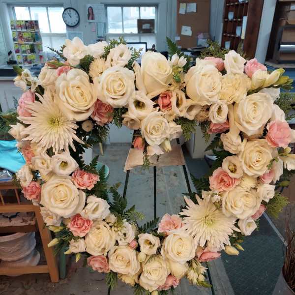 Heart-shaped floral wreath with white roses and pale pink blooms on an easel